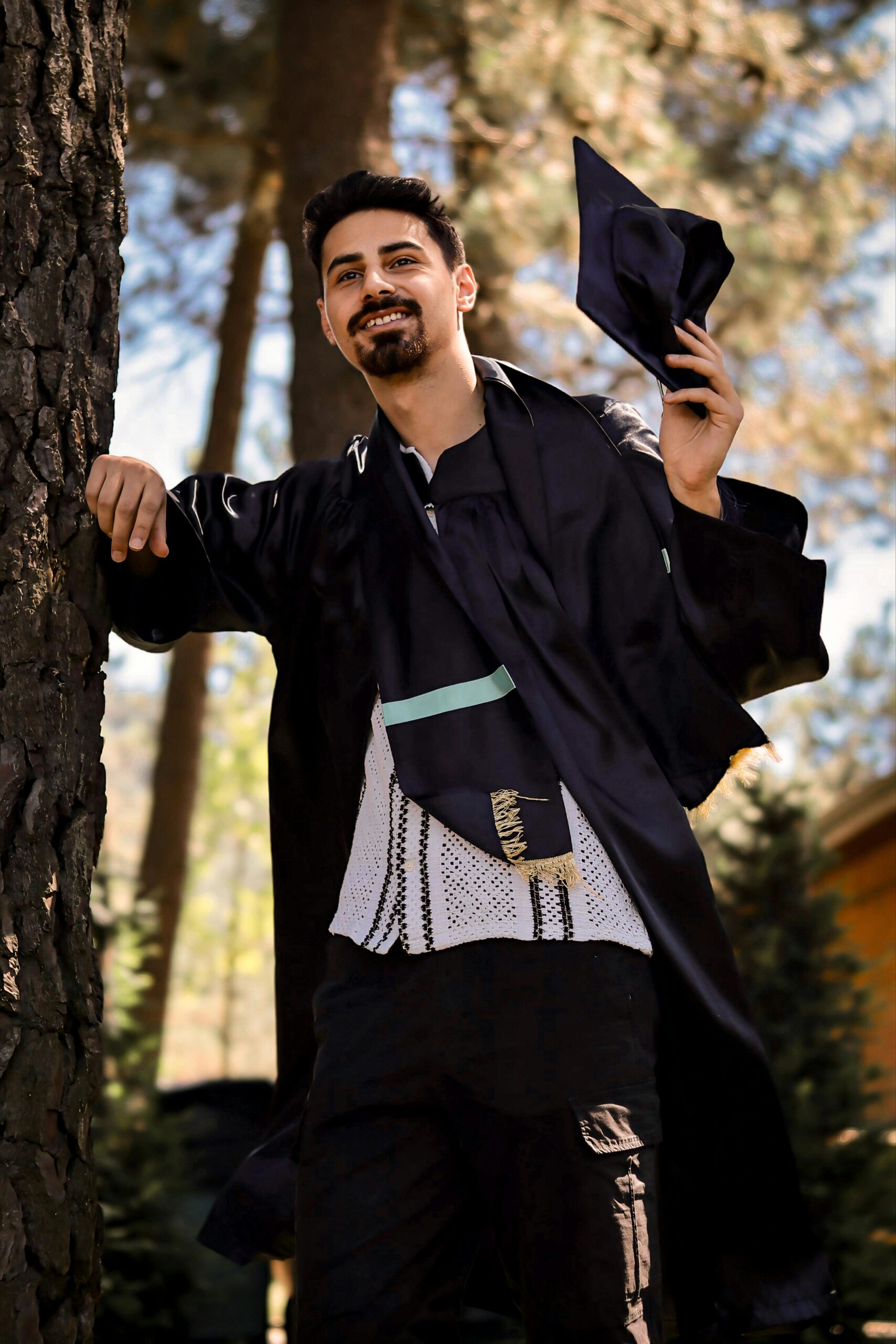 Smiling young male graduate holding a cap outdoors, symbolizing success.